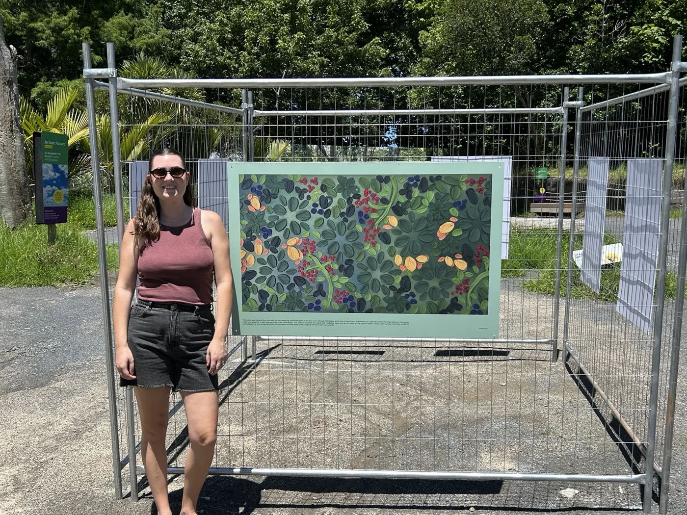 Artist standing with her accepted nature-themed artwork displayed in a zoo art walk